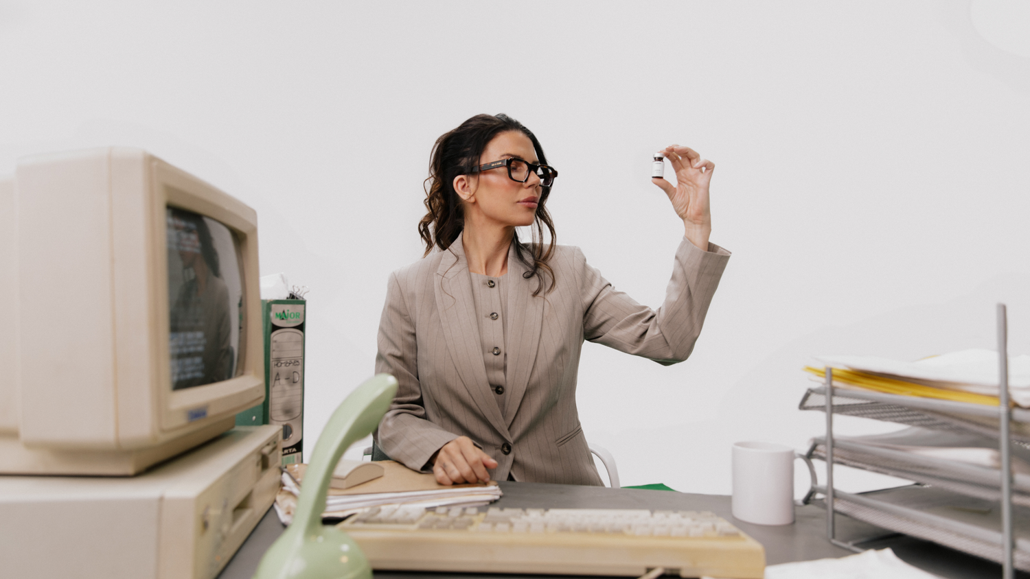 Woman at a retro office desk examining a small GLP-1 medication vial as she weighs her maintenance options