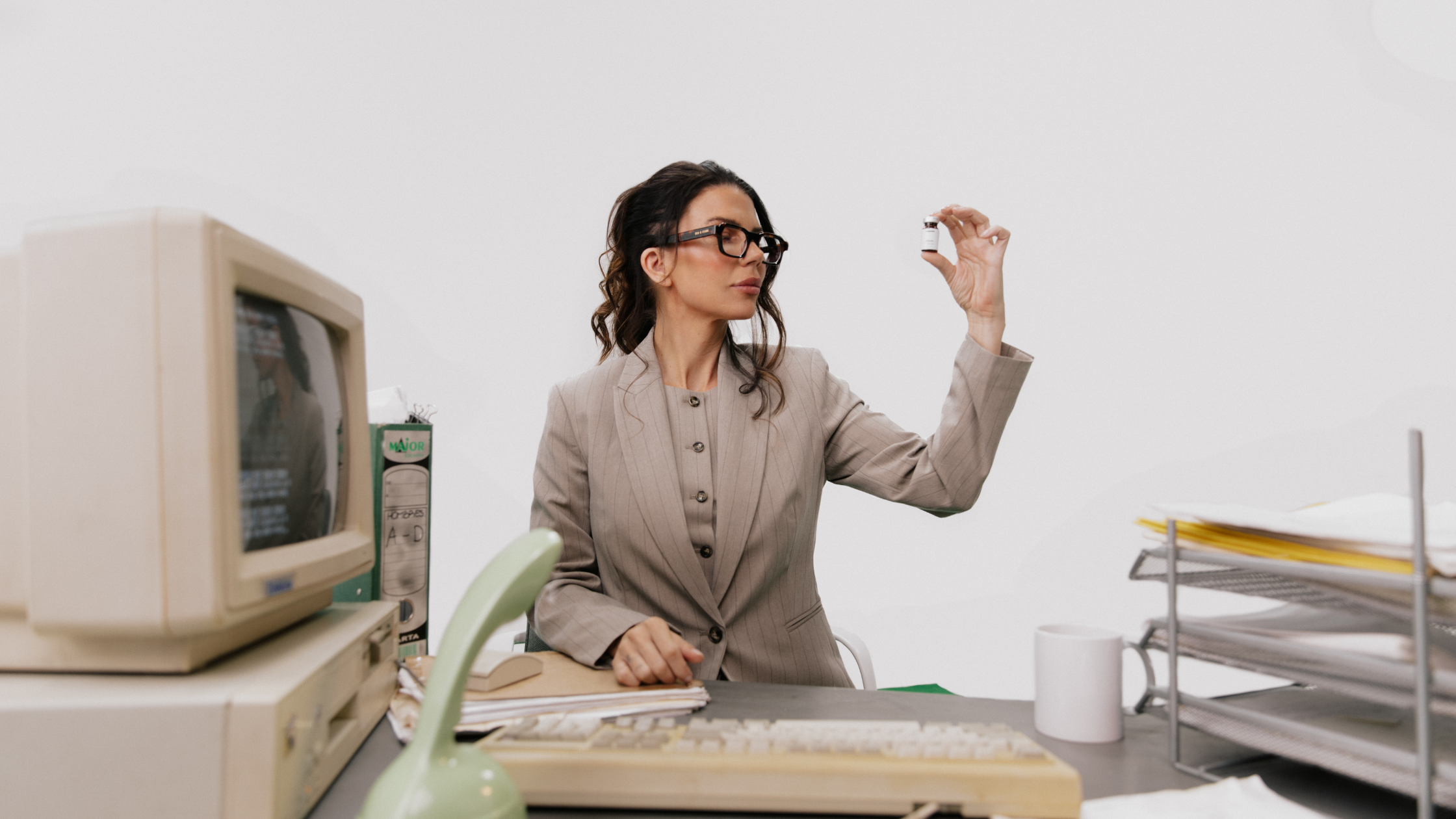 Woman at a retro office desk examining a small GLP-1 medication vial as she weighs her maintenance options