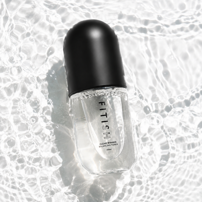 A clear cosmetic bottle with a black cap, labeled FITISH CLEAR MINIS COFFEE, placed on a glossy, wet reflective surface.